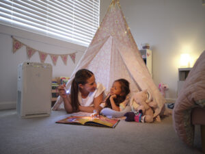 Mother and daughter reading inside a play tent in a child’s bedroom while a Daikin air purifier operates beside them to improve indoor air quality.