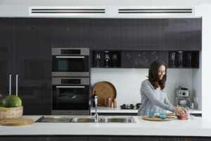 Modern kitchen with a woman preparing food beneath a Daikin ducted air conditioning system integrated into the ceiling for efficient whole-home cooling and heating.